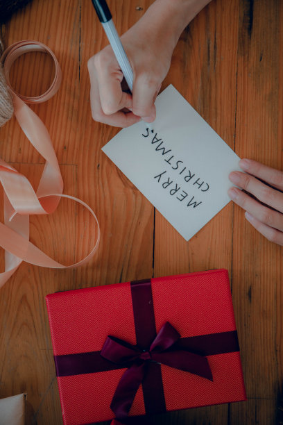 一位女士在圣诞礼品盒中央的手工纸上写字图片下载