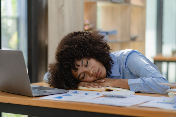 劳累过度的商业女性劳累的年轻女孩在工作期间躺在桌子上使用笔记本电脑和财务图表。图片下载