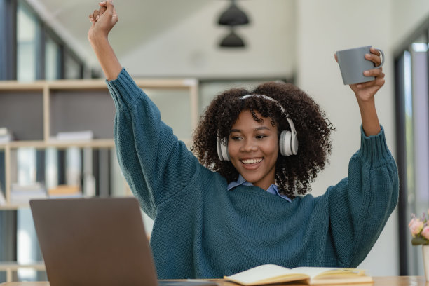 非裔美国女孩用笔记本电脑坐在书桌前写作。努力工作。女子在网上工作时戴着耳机。学生兴奋地在咖啡馆在线学习语言。图片下载