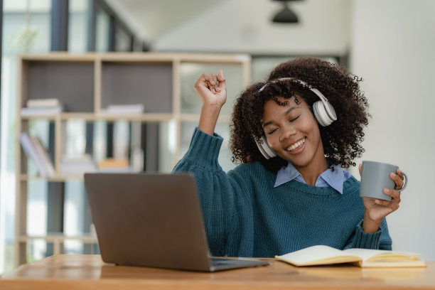 非裔美国女孩用笔记本电脑坐在书桌前写作。努力工作。女子在网上工作时戴着耳机。学生兴奋地在咖啡馆在线学习语言。图片下载
