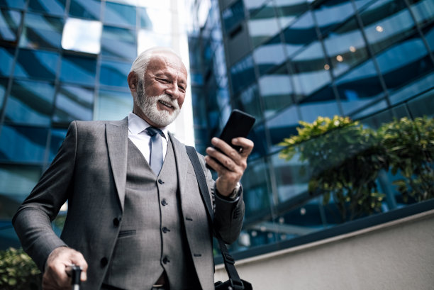 在智能手机上进行专业社交，在商务旅行中站在商业大楼旁边。图片下载
