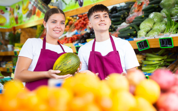 正面快乐微笑的女售货员和穿着围裙的售货员在店里提供新鲜水果图片下载
