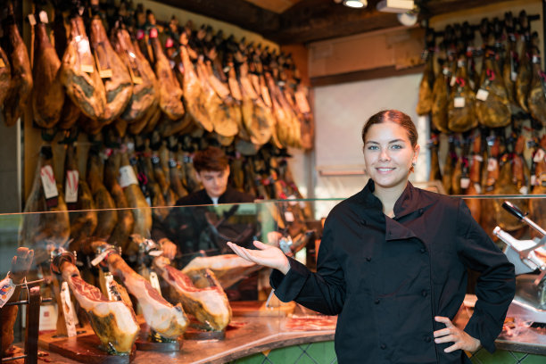 身穿黑色制服的微笑女售货员在肉店推荐伊比利亚火腿图片下载