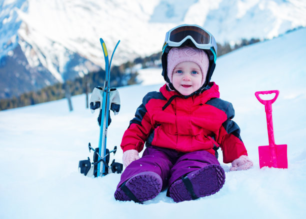 小女孩穿着运动服坐在雪地上，带着小雪板图片下载