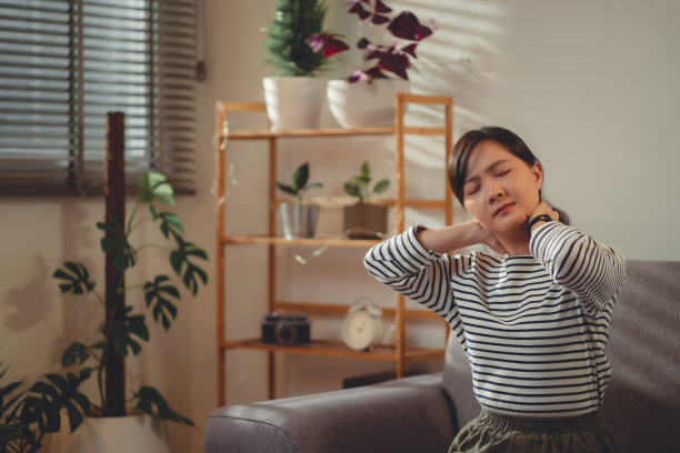 亚洲女性坐在家里客厅的沙发上脖子痛。图片下载