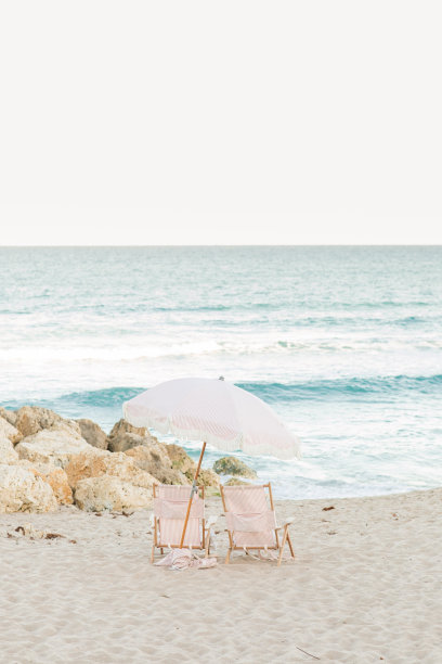 波西米亚条纹粉白色沙滩伞和折叠沙滩椅在棕榈海滩，佛罗里达州日落时分图片下载