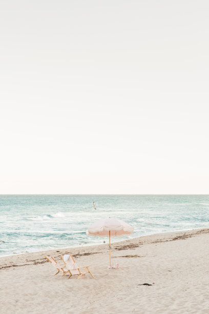 波西米亚条纹粉白色沙滩伞和折叠沙滩椅在棕榈海滩，佛罗里达州日落时分图片下载