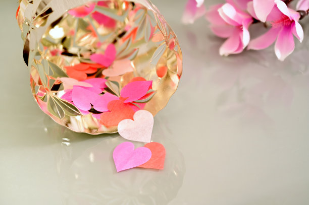 米色玻璃背景上的红色、粉色和白色心形纸从一个银色容器中落下。情人节、母亲节、婚礼贺卡的概念。浪漫的背景，贺卡。图片下载