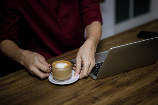 亚洲自由职业者拿着一杯咖啡在工作场所和笔记本电脑在咖啡馆的桌子上图片下载