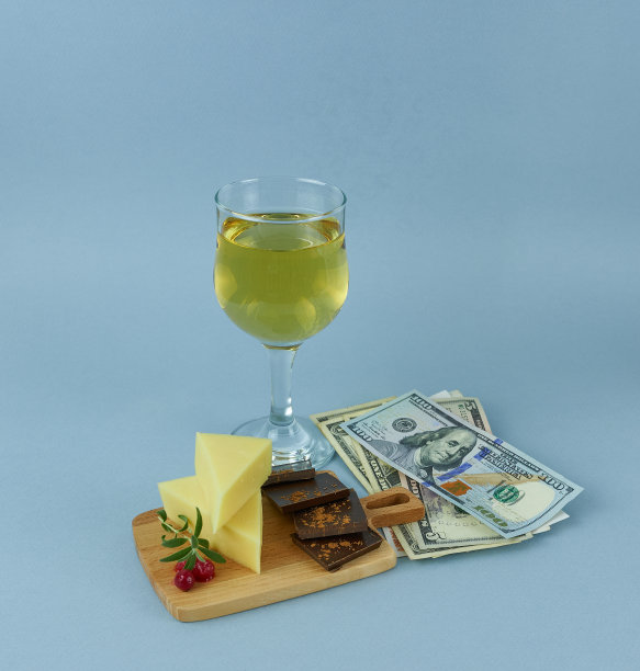 桌上放着一杯白葡萄酒、奶酪和巧克力，旁边放着美钞。图片下载