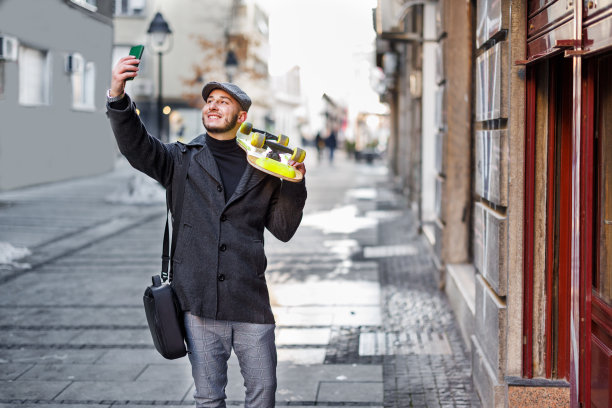 一个年轻人走在城市的街道上，用手机自拍。图片下载