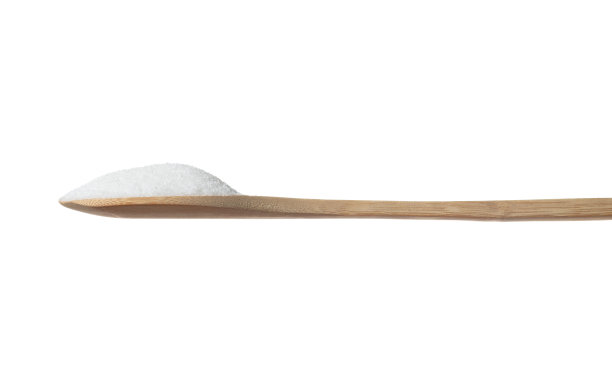 纯精制糖在餐桌勺，白砂糖落线下来。纯精制糖止于空气中，食品对象设计。白色背景隔离高速冻结运动图片下载