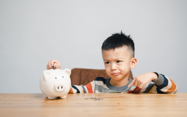 亚洲小男孩在存钱罐里存钱，学习存钱，思考一些事情，孩子为未来的教育存钱。金钱，财务，保险和人的概念图片下载
