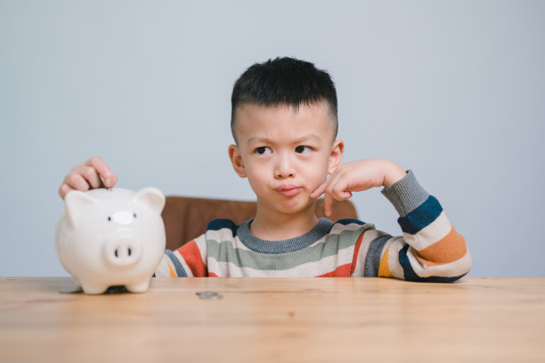 亚洲小男孩在存钱罐里存钱，学习存钱，思考一些事情，孩子为未来的教育存钱。金钱，财务，保险和人的概念图片下载