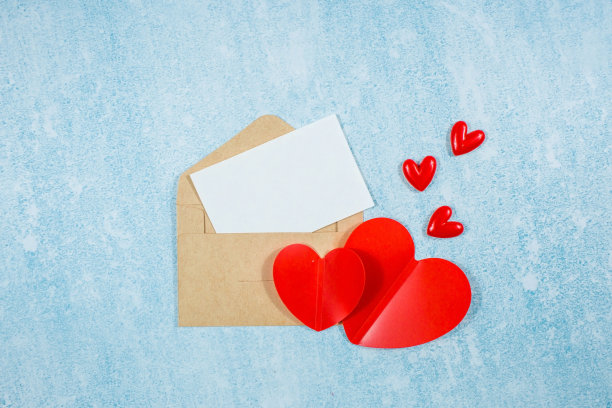 红色的心，一个信封，一张蓝色背景上有复制空间的白纸。情人节节日问候的概念。图片下载