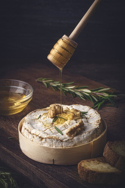 法国奶酪卡蒙贝尔干酪在木盒中烘烤，配以蜂蜜、芳香香草和坚果。法国风味，乡村风格。把蜂蜜倒在奶酪上图片下载