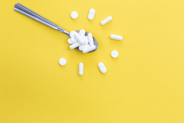 白色药丸在汤匙在一个花的形状在黄色背景，平铺。图片下载