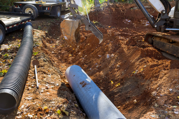在地面操作拖拉机升降机污水管道的工人正在准备安装地下混凝土管道，这是安装过程的一部分。图片下载