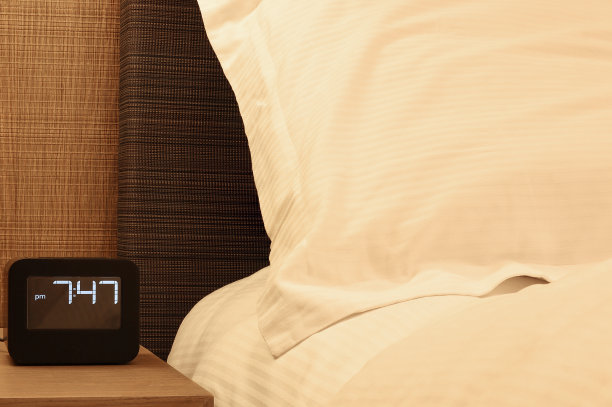 房间的床头柜上放着白色枕头和电子闹钟。放松的概念图片下载