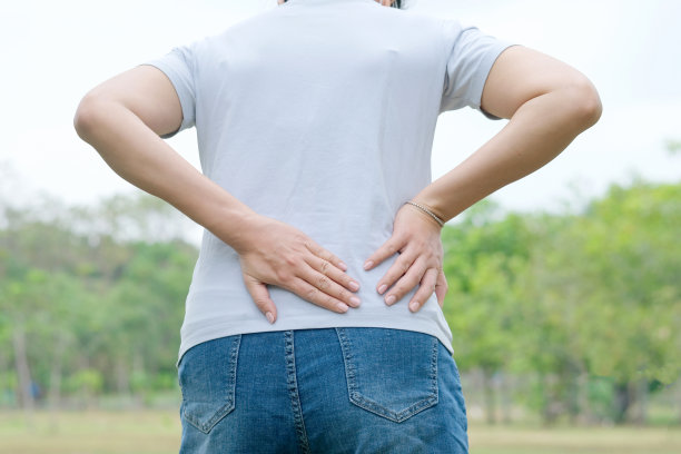 女人的手在公园里，她的腰被夹住了，背部很痛。练习的原因。图片下载
