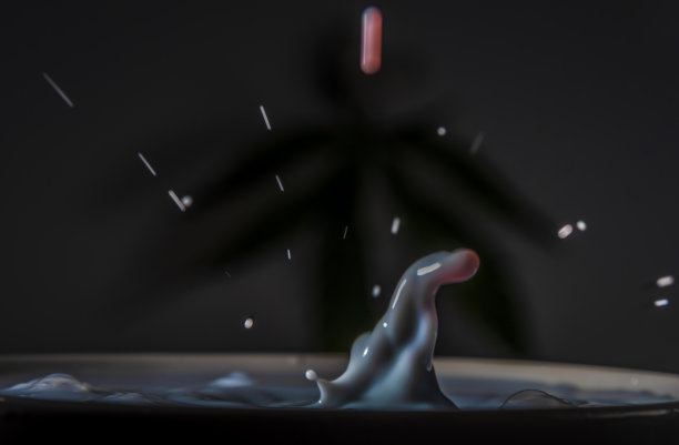 彩色鲜奶滴入另一种颜色的牛奶杯与深色背景图片下载