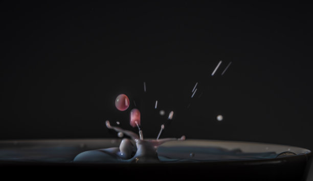 彩色鲜奶滴入另一种颜色的牛奶杯与深色背景图片下载