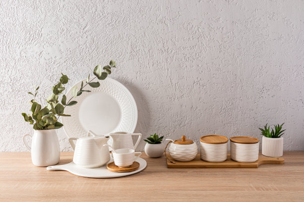 美丽的厨房背景，各种白色的器皿和室内花盆里的花。木制桌面。灰色纹理的墙壁与空间的文本。图片下载