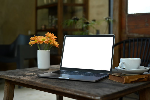 质朴的木桌上放着空空的笔记本电脑、一杯咖啡、书和插着黄花的花瓶。图片下载