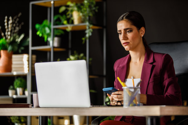年轻的女商人坐在她的办公桌上阅读笔记本电脑上的电子邮件图片下载