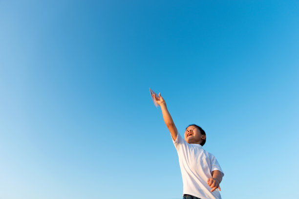 小男孩在蓝天下扔纸飞机图片下载