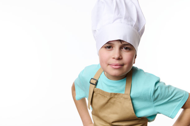 一个戴着厨师帽和围裙的少年的白色孤立的肖像，手牵在腰带上，微笑着看着相机图片下载