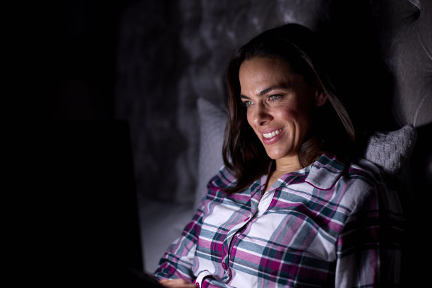 晚上坐在床上用笔记本电脑微笑的女人图片下载