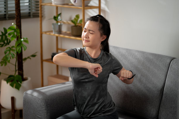 亚洲妇女坐在家里客厅的沙发上遭受背痛。图片下载