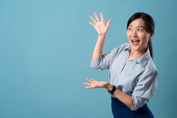 亚洲妇女快乐的微笑显示和看着空白复制空间孤立在蓝色背景。图片下载