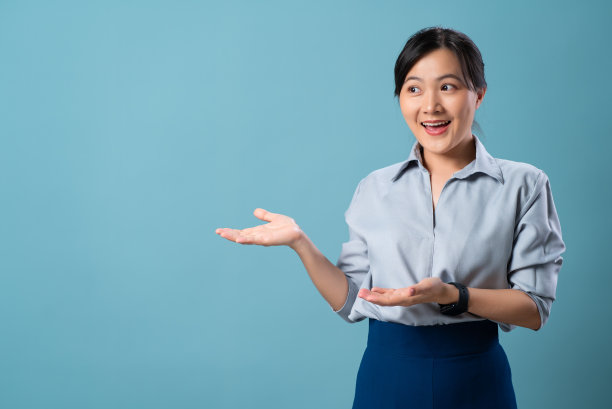 亚洲妇女快乐的微笑显示和看着空白复制空间孤立在蓝色背景。图片下载