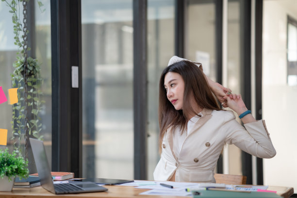 年轻的女商人伸展手，坐在办公室的椅子上。图片下载