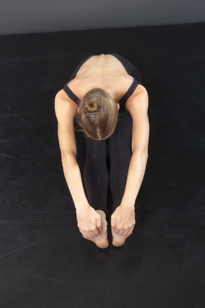 穿着黑色连体衣的年轻女子，在黑色地板上伸展身体。图片下载