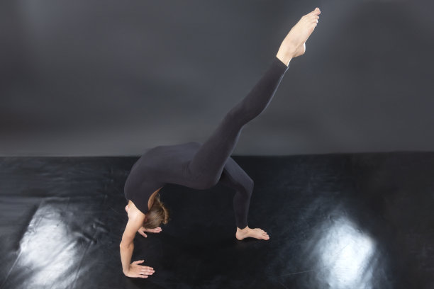 年轻女子在一个黑色连体衣，做轮瑜伽姿势。图片下载