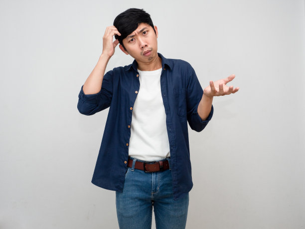 亚洲男人站着挠头，感到怀疑和困惑图片下载