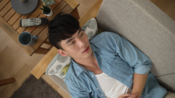 一位亚洲男性玩家躺在家里的沙发上玩手机游戏，输掉比赛后，沮丧地收起智能手机图片下载