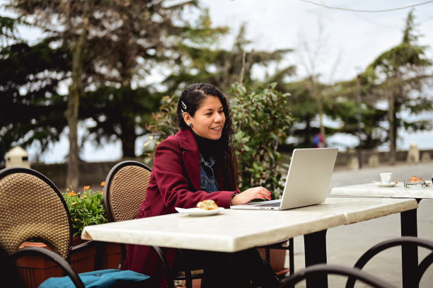 教练博主在冬天或秋天的时候在路边咖啡馆的笔记本电脑上打字。图片下载