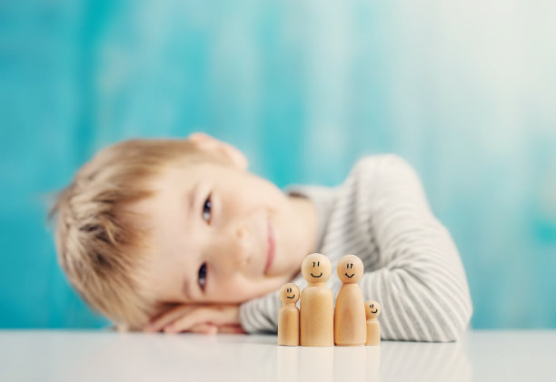 可爱的男孩坐在桌子上，上面有家庭的木制人物。图片下载