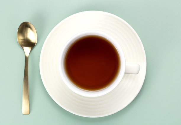 一杯黑色的热茶，勺子放在绿色背景上。前视图。图片下载