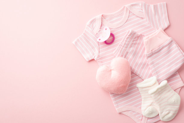 婴儿送礼会的概念。婴儿衣服粉红色紧身裤袜子奶嘴和毛绒心形玩具在孤立的粉彩粉红色背景与复制空间的俯视图照片图片下载