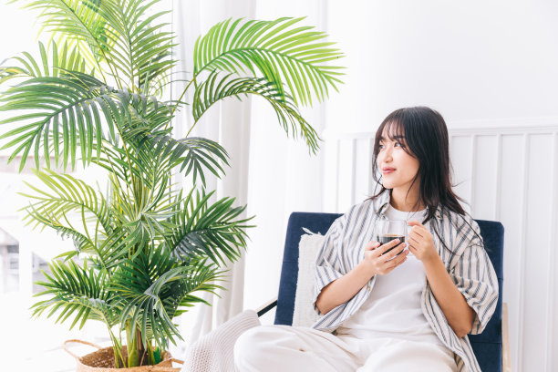 年轻漂亮的女人在现代起居室的椅子上微笑，喝着热咖啡，享受舒适家中的安静时光和室内环境图片下载