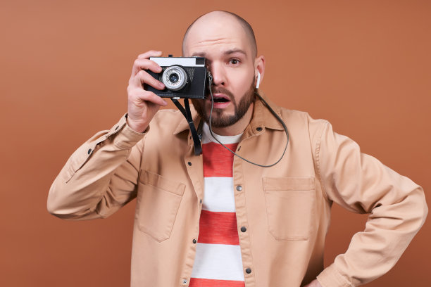 惊奇的年轻人拿着棕色背景的相机。图片下载