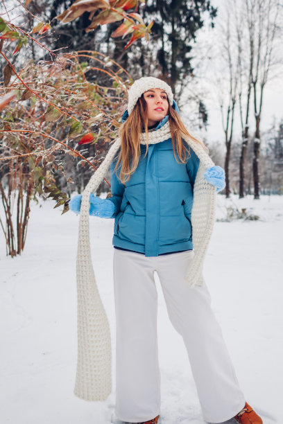 全身画像的年轻女子走在雪的冬天公园穿着蓝色外套，针织温暖的衣服。图片下载