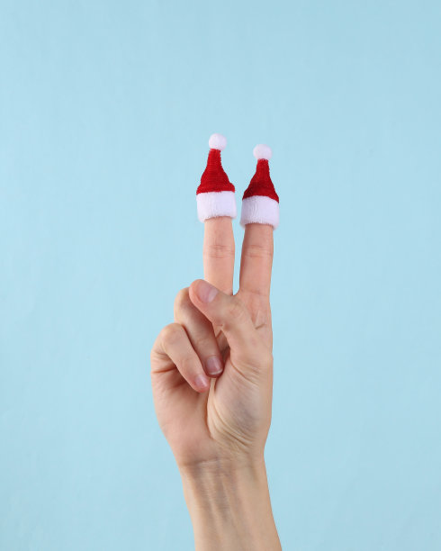 迷你圣诞老人帽子上的手指上的女性手在蓝色的背景。圣诞节的概念图片下载