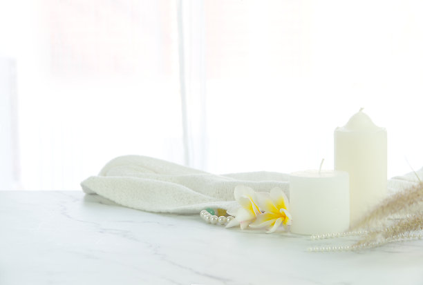 豪华的白色大理石桌面在明亮的房间。装饰蜡烛，鸡蛋花和白色织物与模糊窗帘的窗口背景复制空间图片下载