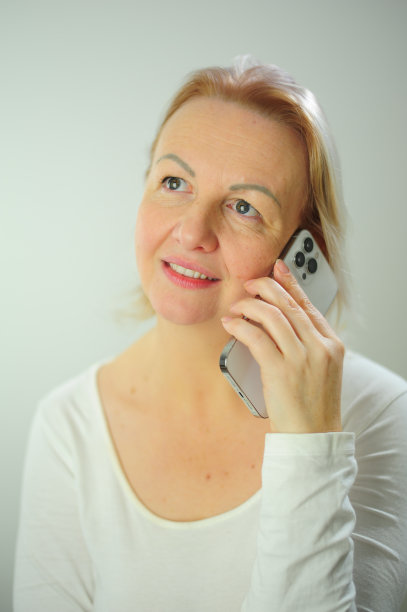 女人在家里打电话的特写照片，微笑的成年女人打电话，看着白色t恤，金发，白色电话图片下载